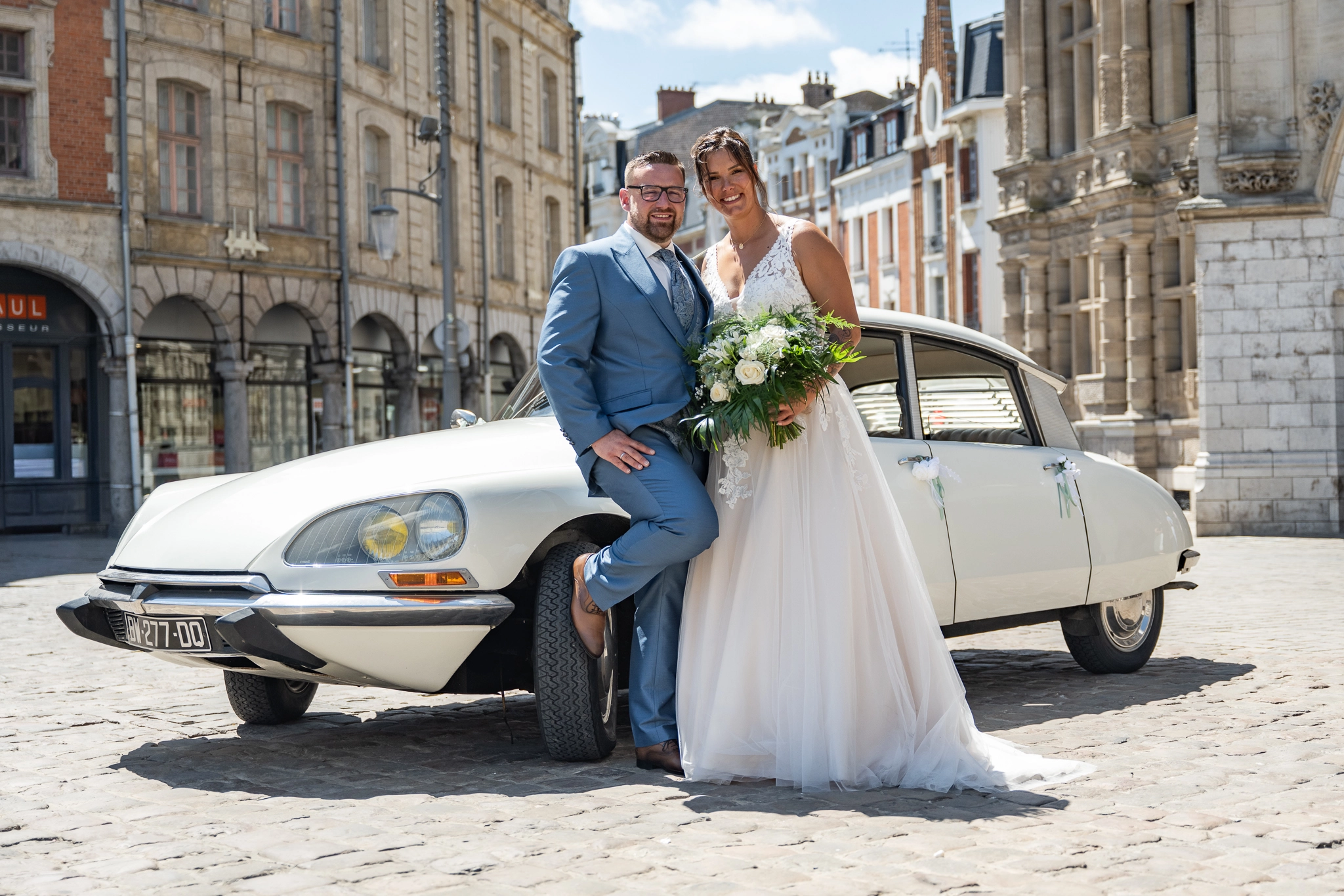 Photo de mariage avec les mariés devant une Citroën DS ancienne et le beffroi d'Arras